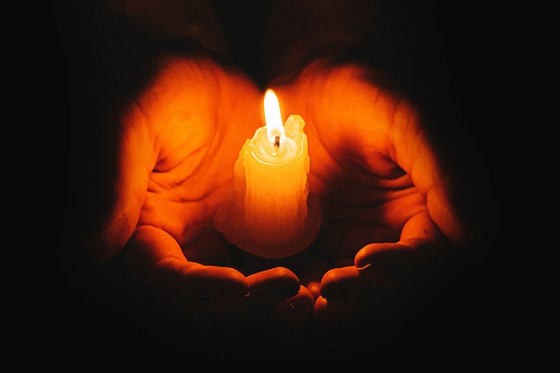 Hands holding a lit candle in darkness, symbolizing hope and God’s presence during the pain and suffering of estrangement .